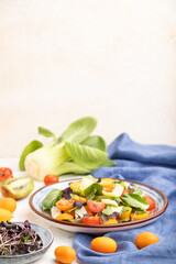 Vegetarian salad of pac choi cabbage, kiwi, tomatoes, kumquat, microgreen sprouts on a white concrete background. Side view, selective focus, copy space.