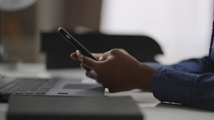 young black woman is using modern mobile phone in working place, closeup of hands with gadget, checking news and message in social nets