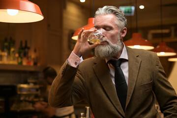 solid gray-haired man drinking his whiskey in a night bar