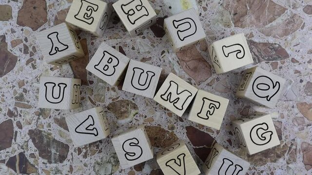 Bumf - concept with alphabet letters on wooden blocks arranged to the centre with a frame of random letters on cubes over a stone background. Rotating table