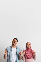 Nice Offer. Excited Muslim Couple Looking And Pointing Up At Copy Space
