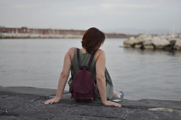 Fototapeta na wymiar Young pretty woman sitting alone on the pier near the sea, looking on the water and waiting