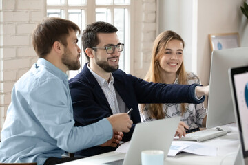 Smiling multiracial colleagues gather at workplace look at PC screen brainstorm cooperate together. Happy diverse businesspeople look at computer screen discuss business project. Teamwork concept.