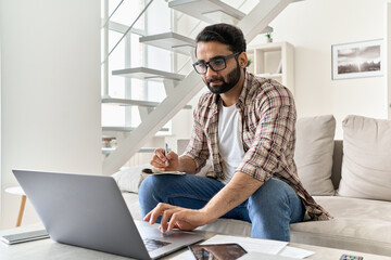 Young indian man student or distance employee working online from home office, e learning using laptop computer watching remote webinar training class, having virtual video call meeting in homeoffice.