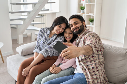 Happy indian family with teen child daughter having fun taking selfie on modern smartphone at home. Smiling parents and teenage kid bonding looking at mobile phone posing for family photo sit on sofa.