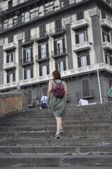 Photo from back of young woman  wearing summer dress and bag walking up stairs in old town 
