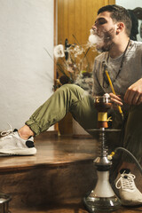 Young handsome guy smoking hookah alone closeup. Hookah and sparks from coals. Shisha, spark, hookah sparks. Young man smokes a fragrant oriental hookah.