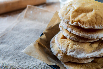 Stack of homemade pita bread. Freshly baked gluten-free pita bread on a rustic cloth, hot from the oven. Round flatbread that can be stuffed with food. Rolling pin and flour in a wooden background