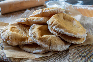 Stack of homemade, fluffy, pita bread. Freshly baked gluten-free pita bread on a rustic cloth, hot from the oven. Round flatbread that can be stuffed with food. Rolling pin and flour in the background