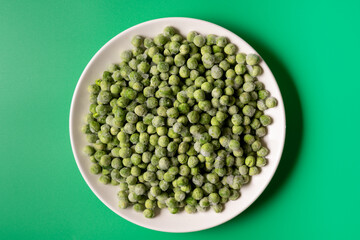 Frozen green peas in a bowl on green background.