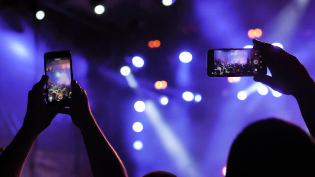 People hands silhouette taking photo or recording video of live music concert with smartphone. Bright colorful stage lighting. Nightlife, technology, photography, entertainment concept