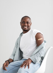 Happy black man showing his arm with an adhesive bandage after injection of vaccine.