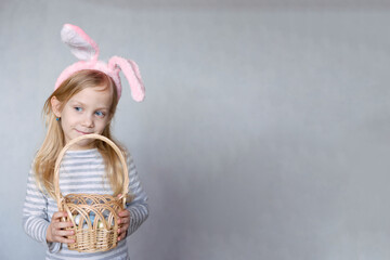 blonde girl in a striped jacket, on a bright background, with rabbit ears on her head, holding a basket of eggs, smiling looks to the side