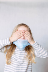 blonde girl in striped jacket and medical mask covered her face with her hands