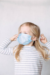 blonde girl in striped jacket and medical mask removes mask with hands, unfocus