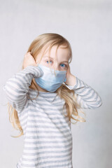 Blonde girl in striped jacket and medical mask removes closed ears with her hands