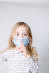 Blonde girl in striped blouse and medical mask removes the index finger to her lips