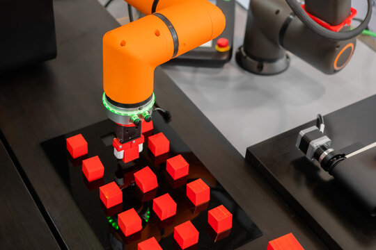 Orange pick and place robotic clamp arm manipulator moving red toy blocks at modern robot trade show, exhibition. Manufacturing, engineering, industrial, ai, automated technology concept