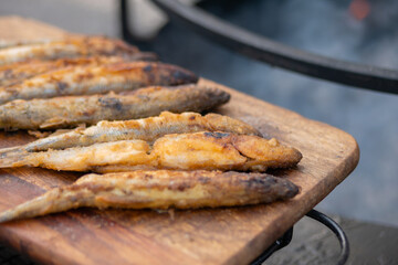 Crispy breaded european smelt fish on wooden cutting board at summer outdoor food market: close up. Seafood, barbecue, gastronomy, cookery, street food concept