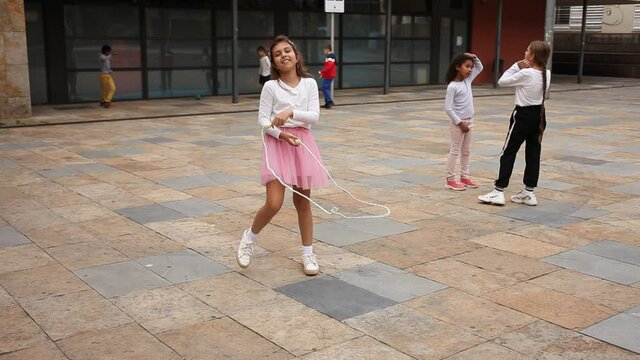 Cheerful sporty tween girl jumping rope in school yard during recess in warm autumn day. High quality FullHD footage