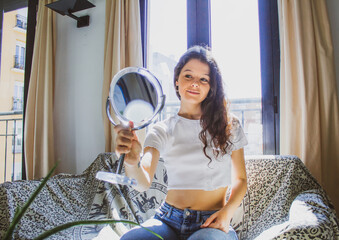 young woman with makeup looking at herself in a mirror on the sof