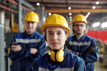 Young serious female worker of large industrial plant or factory in workwear and protective helmet...