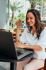 Freelance concept. Attractive girl uses her laptop while sitting in a cafe on the street