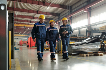Group of workers or engineers of contemporary industrial plant moving along large workshop with...
