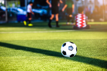 Selective focus to soccer ball on green artificial turf with blurry soccer team is training. Sport...