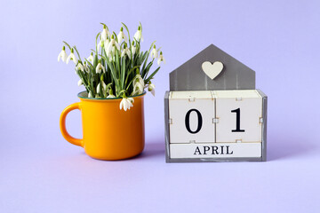 Calendar for April 1: cubes with the numbers 0 and 1, the name of the month of April in English, a bouquet of snowdrops in a yellow tea cup on a blue background