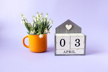 Calendar for April 3: cubes with the numbers 0 and 3, the name of the month of April in English, a bouquet of snowdrops in a yellow tea cup on a blue background