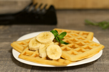 Viennese waffles with banana and mint leaf. Delicate homemade Belgian waffles on a white plate in the kitchen.