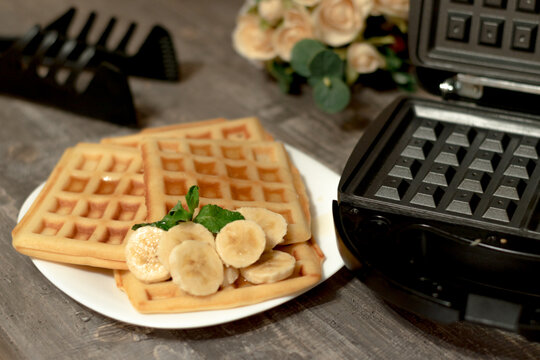 Viennese waffles with banana and mint leaf. Delicate homemade Belgian waffles on a white plate in the kitchen.