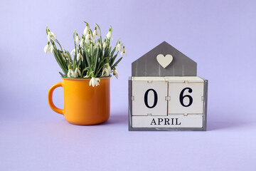 Calendar for April 6: cubes with the numbers 0 and 6, the name of the month of April in English, a bouquet of snowdrops in a yellow tea cup on a blue background