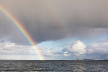 dark sea and passing rain front rainbow with the clear sky and island with the lighthouse silhouette in the background