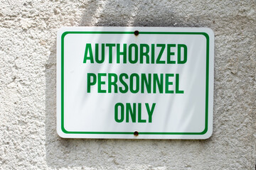 A white rectangular sign with green bold capital letters and a green border drilled to a concrete wall stating only authorized personnel may enter the premises. Bridgetown, Barbados, March 2021. 