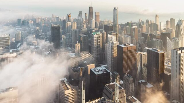 Incredible panning up aerial skyline time lapse as patches of dense low fog makes its way into the heart of downtown Chicago and over Lake Michigan surrounding the highrise buildings at sunrise.