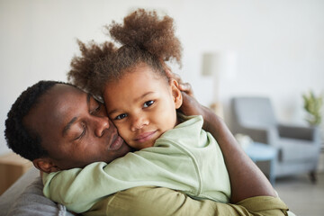 Portrait of cute African-American girl embracing father and looking at camera in cozy home...
