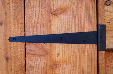 Wrought iron black t-hinge on wooden shed door.