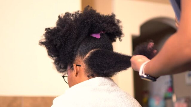 African American mother styling her beautiful teenage daughter's hair in a home salon or kitchen