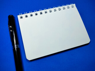 Selective focus of pen and notebook on blue background with copy space.