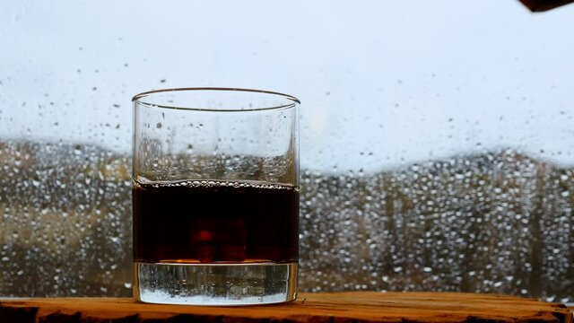 Whiskey on the bar in the rain window. Pour whiskey at the bar. A glass of whiskey with ice by the window with rain.