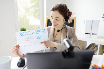 Young woman is teaching english with laptop computer, camcorder and headphone online at home....