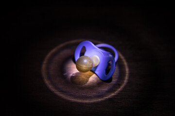 Baby pacifier on wooden table with low key toned background.