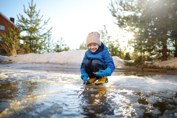 Cute preschooler boy is playing with a stick in brook on sunny day. Child having fun and enjoy a big puddle. All kids love play with water. Happy childhood. Outdoor activity for baby in sping