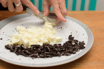 Hands chopping white chocoloate to melt and cookies to prepare easter eggs