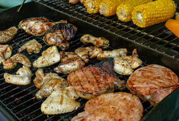 A barbecue with pork chops, chicken wings and thighs, sausages, vegetables and corn.