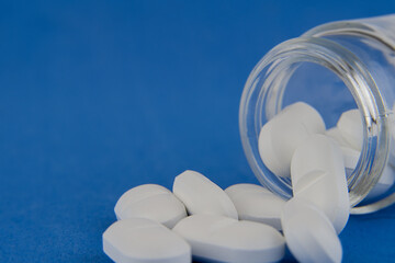 White tablets in a glass bottle on a blue background