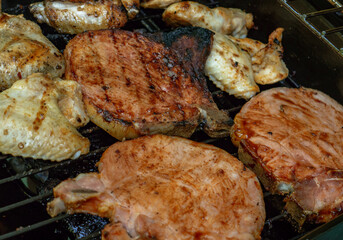 A barbecue with pork chops, chicken wings and thighs, sausages and vegetables 