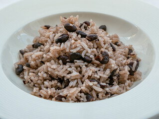 Rice with black beans served in a white bowl on a white tablecloth, widely consumed in the Dominican Republic and known as moro.